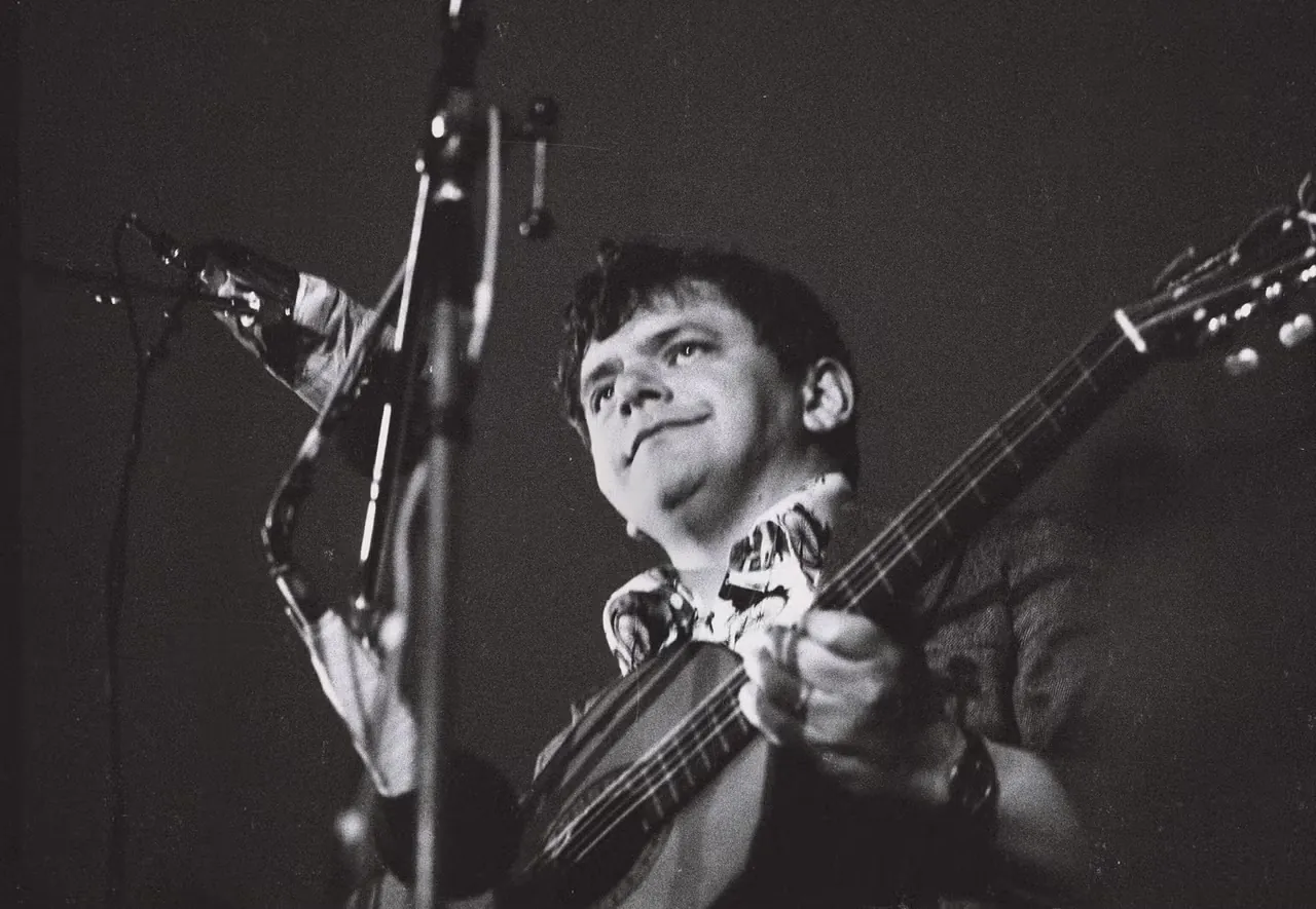 Fred Åkerström sjunger och spelar gitarr vid en mikrofon, svartvitt scenfoto.